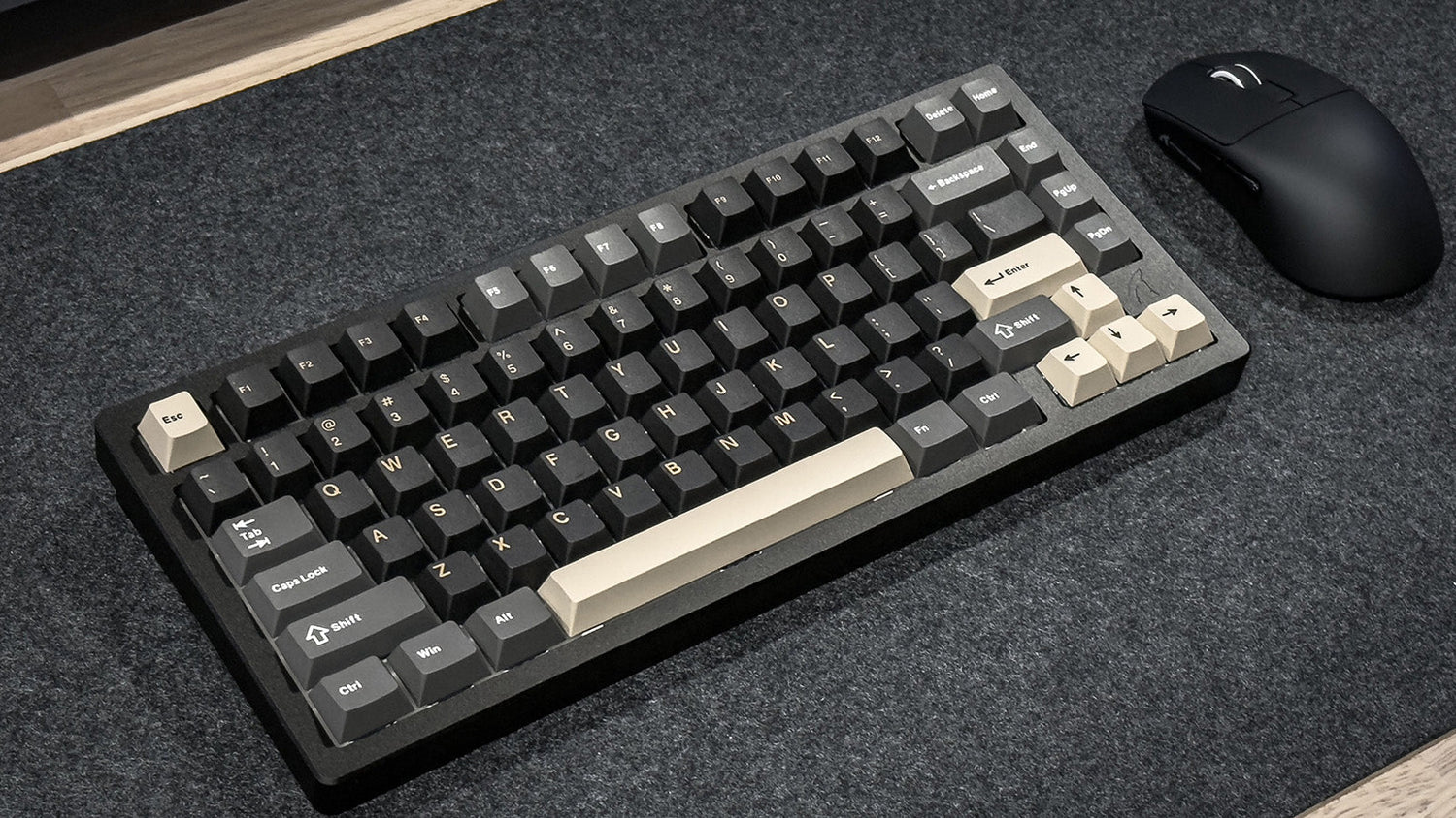 A black 60% mechanical keyboard with dark keycaps and cream-colored accent keys on the arrow cluster and Enter key, paired with a white wireless mouse on a dark textured desk mat